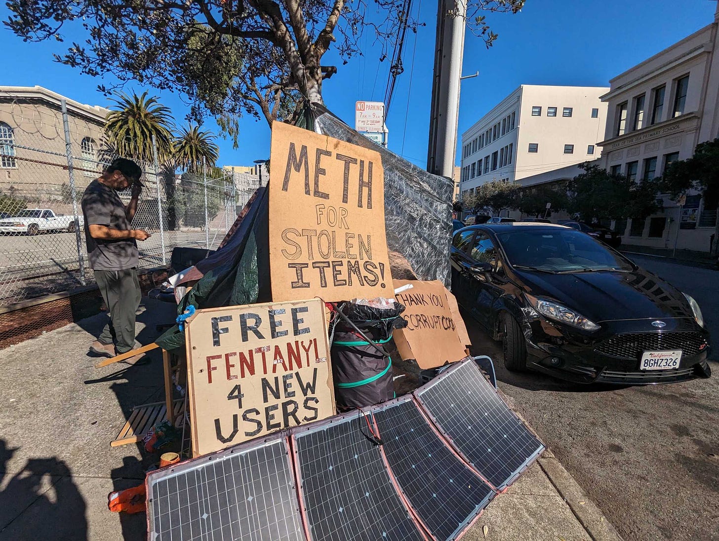 Signs reading "Meth for stolen items" and "free fentanyl 4 new users" sit atop Joseph Adam Moore