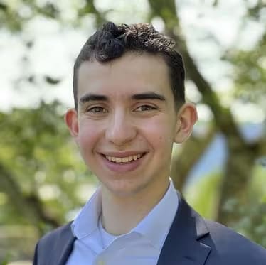 A young man in a dress shirt smiles at the camera.